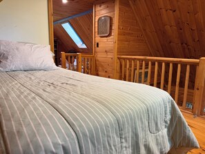 A bedroom with a bed, a window, and a wooden balcony railing.
