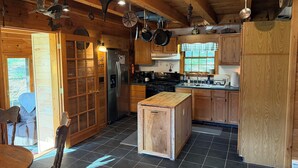 Une cuisine rustique, située dans une cabane en bois, équipée d’un réfrigérateur, d’une cuisinière et de meubles de rangement en bois.