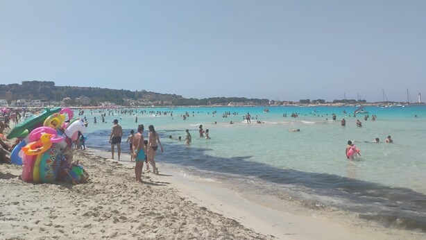 A beach with people swimming and walking along the shore. There are colorful inflatable toys on the sand.