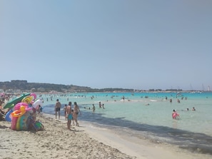 A beach with people swimming and walking along the shore. There are colorful inflatable toys on the sand.