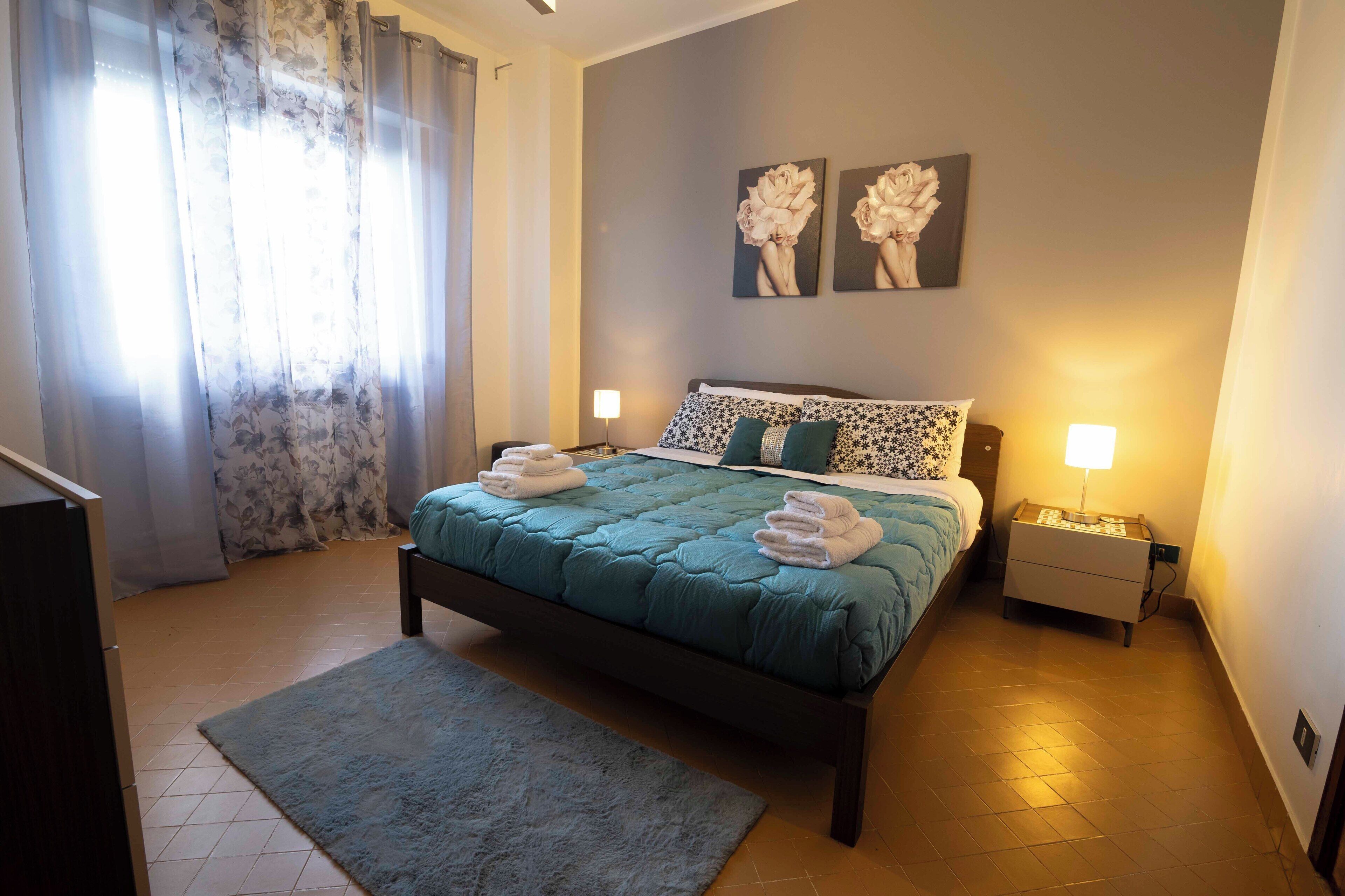 Une chambre à coucher bien rangée, avec un lit, deux tables de chevet, une commode et une grande fenêtre avec des rideaux.