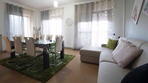 A living room with a dining area, a sofa, a green rug, and a clock on the wall.