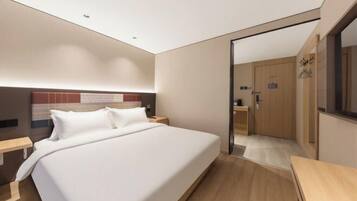 A modern hotel room with a large bed, wooden flooring, a nightstand, and a door leading to another room.
