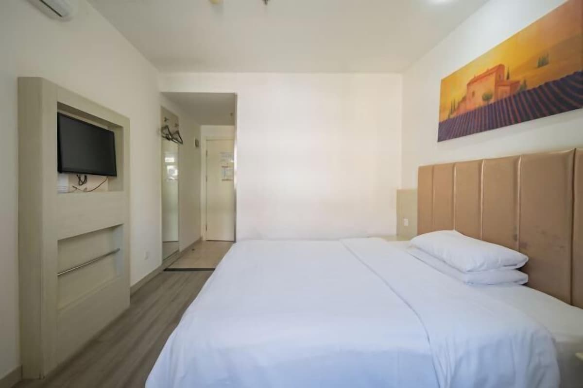 A hotel room with a bed, a TV mounted on the wall, and a painting above the bed.
