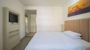 A hotel room with a bed, a TV mounted on the wall, and a painting above the bed.