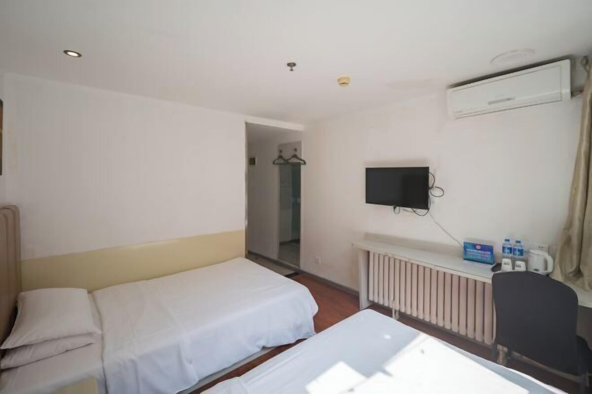 A hotel room with two single beds, a TV mounted on the wall, a radiator, and a chair.