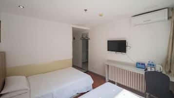 A hotel room with two single beds, a TV mounted on the wall, a radiator, and a chair.