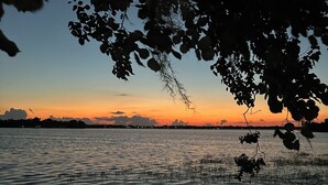 A sunset over a calm body of water with silhouettes of trees and distant city lights. - Cozy 1 Bedroom home on Beautiful Lake Alfred (Lake Alfred)