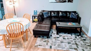 A living room with a sectional sofa, a coffee table, a dining table with chairs, a wall clock, and a framed picture. - Cozy 1 Bedroom home on Beautiful Lake Alfred (Lake Alfred)
