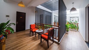 Un interior moderno con suelo de madera, una zona de estar con sillas naranjas, una mesita y un balcón con plantas.