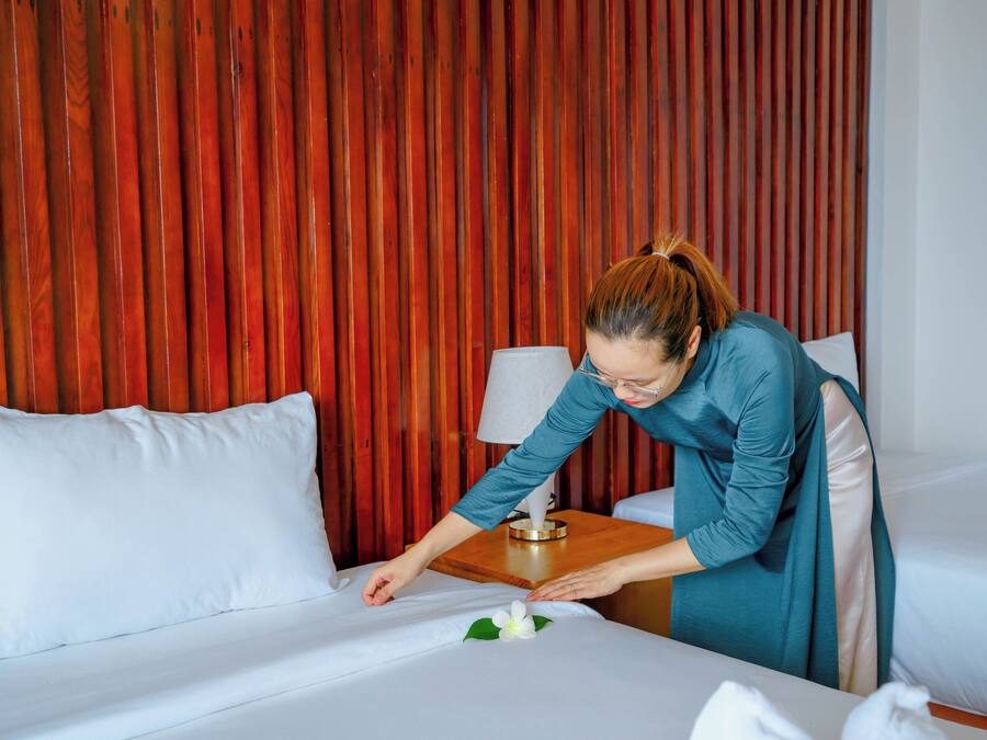 A hotel room with a wooden slat wall, a bed with white bedding, and a bedside table with a lamp.