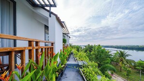 Un balcón con vistas a un lago, rodeado de vegetación y un edificio blanco.