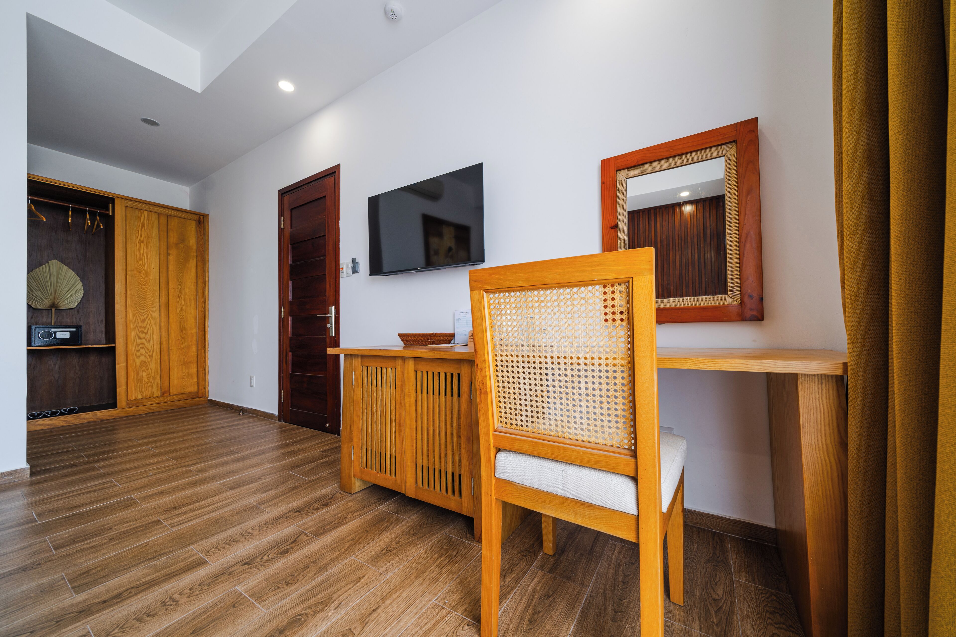 Ein Zimmer mit Holzboden, einem Holzschrank, einem an der Wand befestigten Fernseher und einem Spiegel über einem Holztisch.