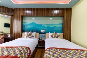 Habitación de hotel con dos camas, un mural de montañas, cabecera de madera y una mesita con un teléfono y una botella.