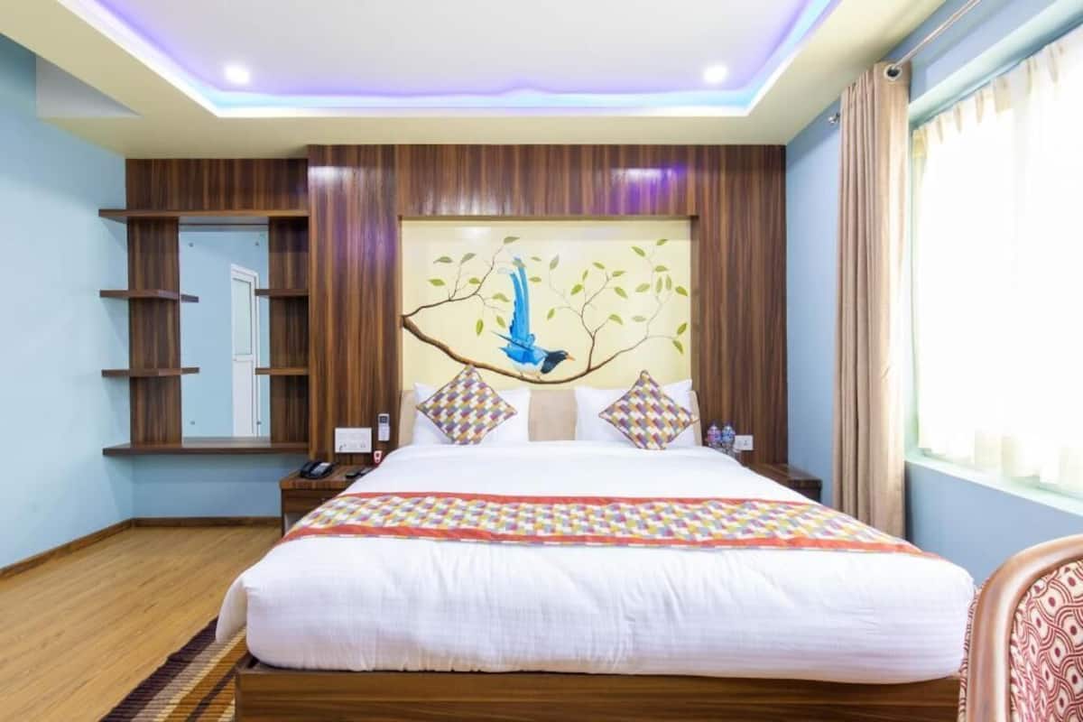 Ein Hotelzimmer mit einem großen Bett, einer Wandablage, einem Vogelbild auf einem Ast und einem Fenster mit Vorhängen.