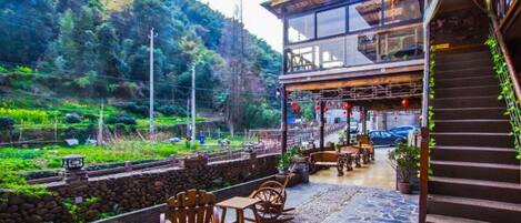 A restaurant with outdoor seating, a staircase, and a view of a green hillside.