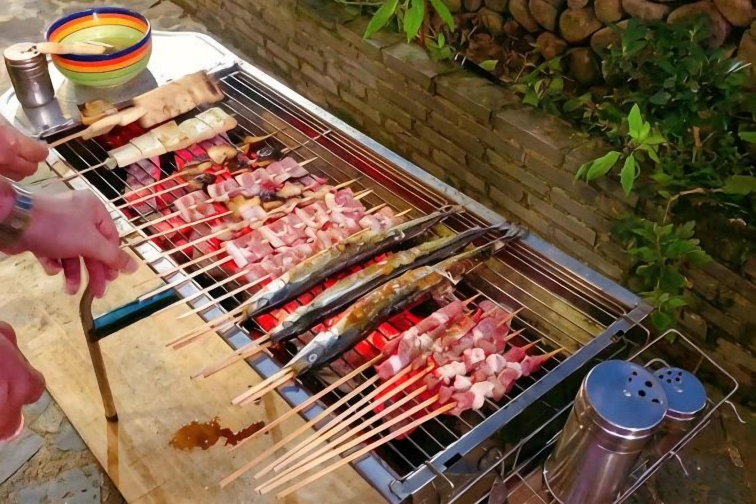 Een barbecue met spiesen vlees en vis, een metalen bak en een houten plank.