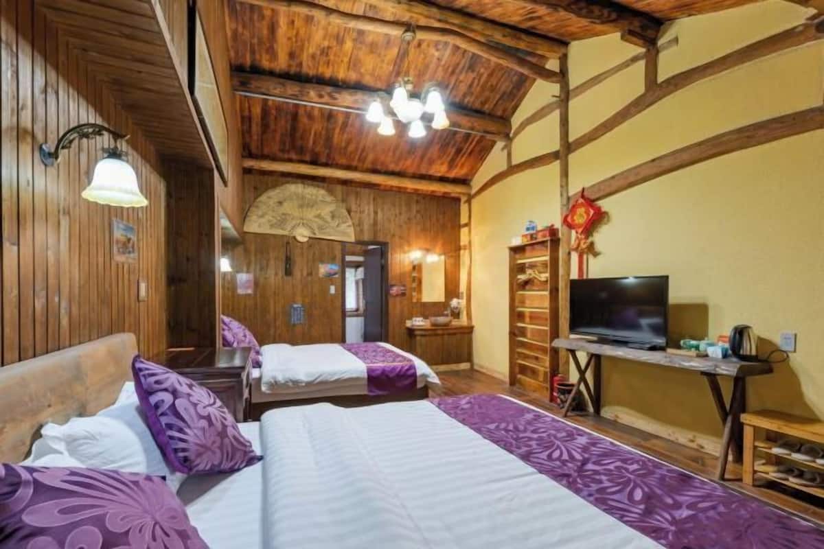 A wooden-floored room with two beds, a TV, and a fan.