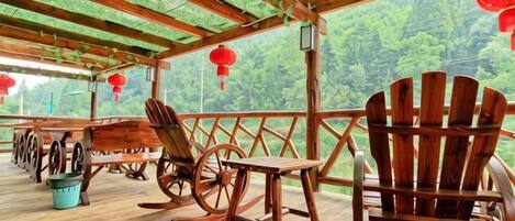 Une terrasse en bois, avec une chaise et une table en bois, entourée d’une rambarde et offrant une vue sur une zone boisée.