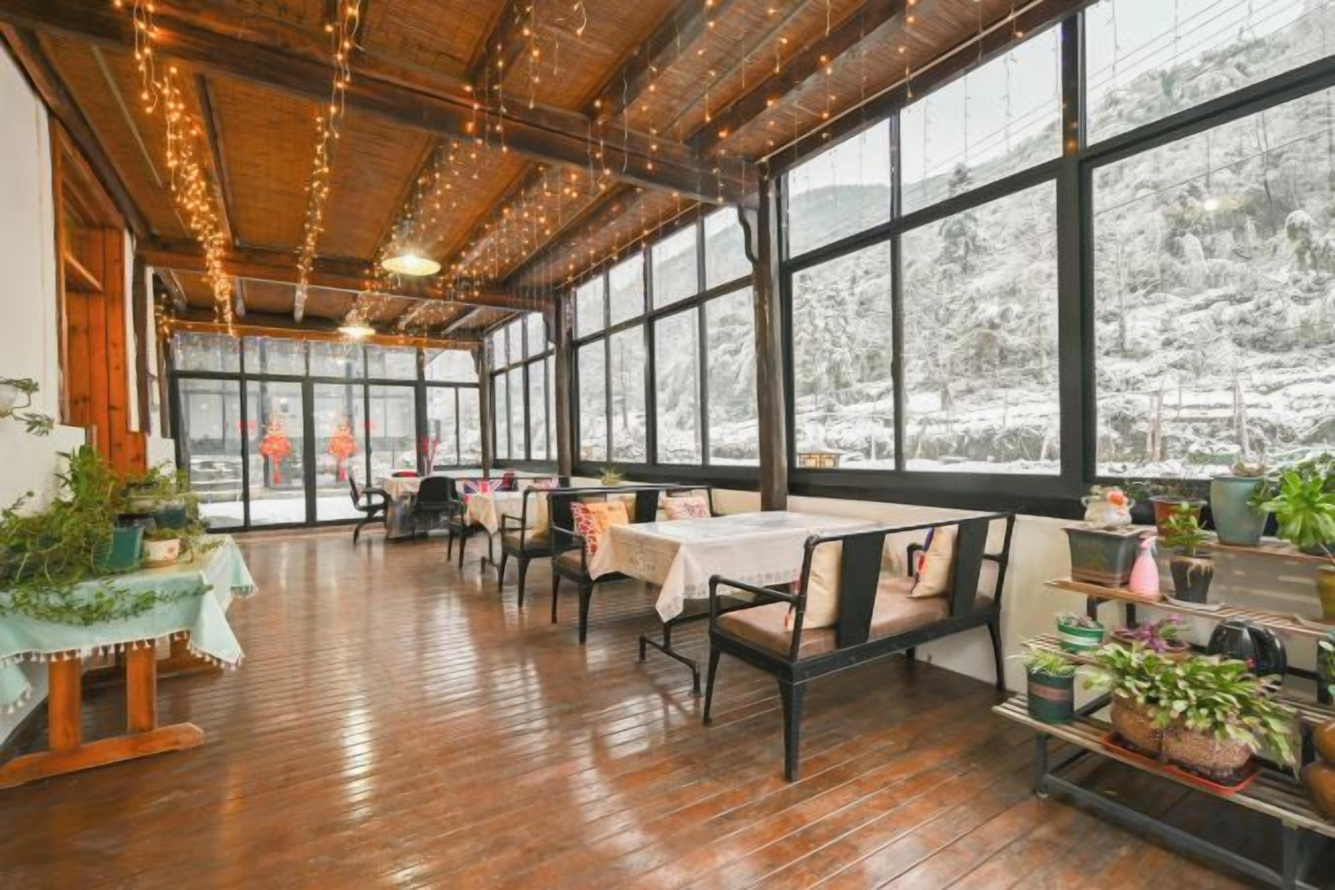 A restaurant with wooden flooring, tables with white tablecloths, and large windows offering a view of snow-covered trees.