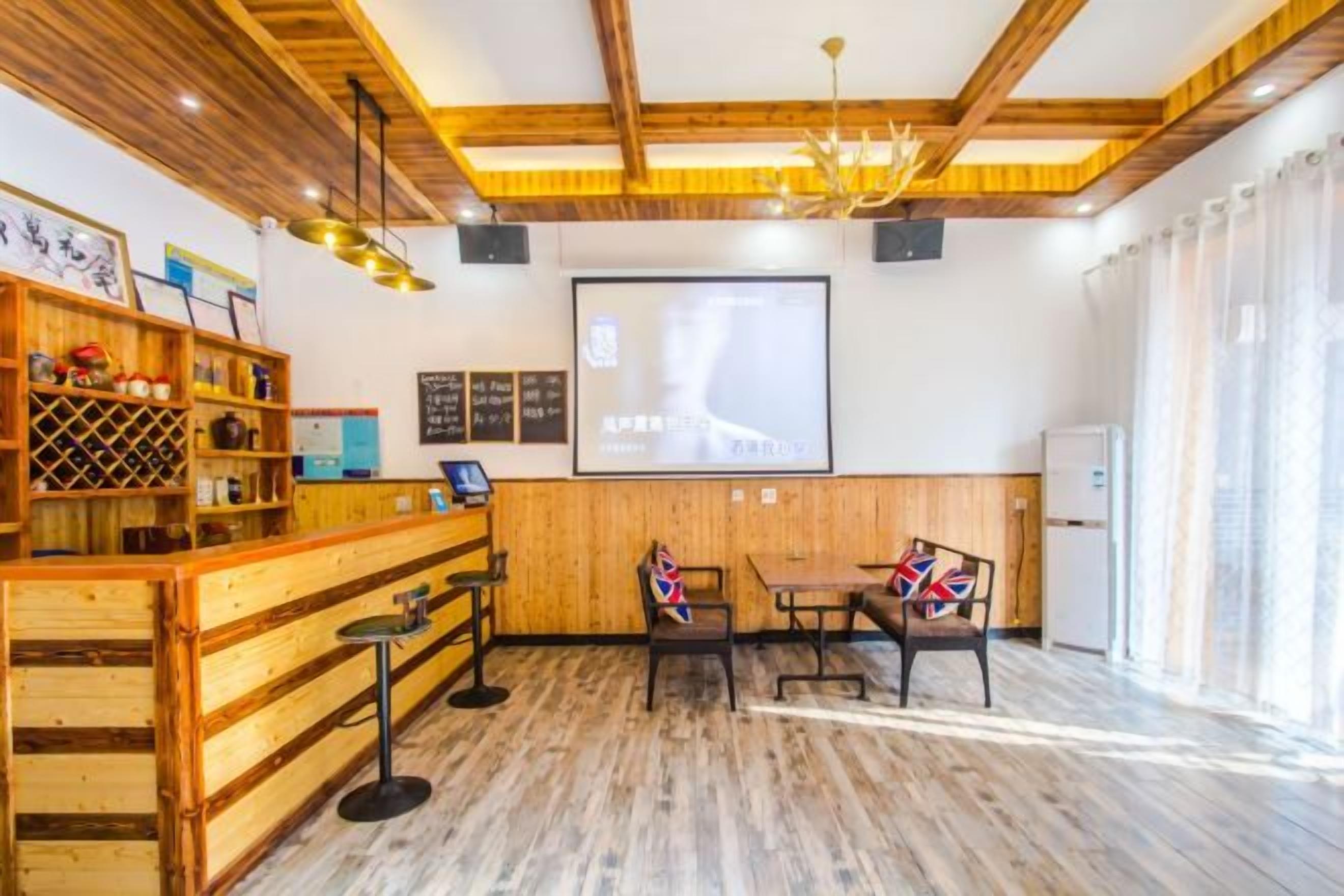 Una habitación con techo de madera, una zona de bar con taburetes, una pantalla de proyector y una pizarra.