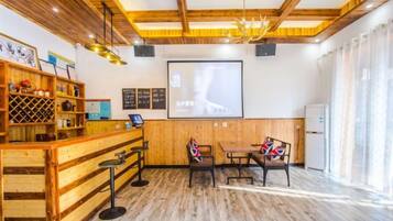 Una habitación con techo de madera, una zona de bar con taburetes, una pantalla de proyector y una pizarra.