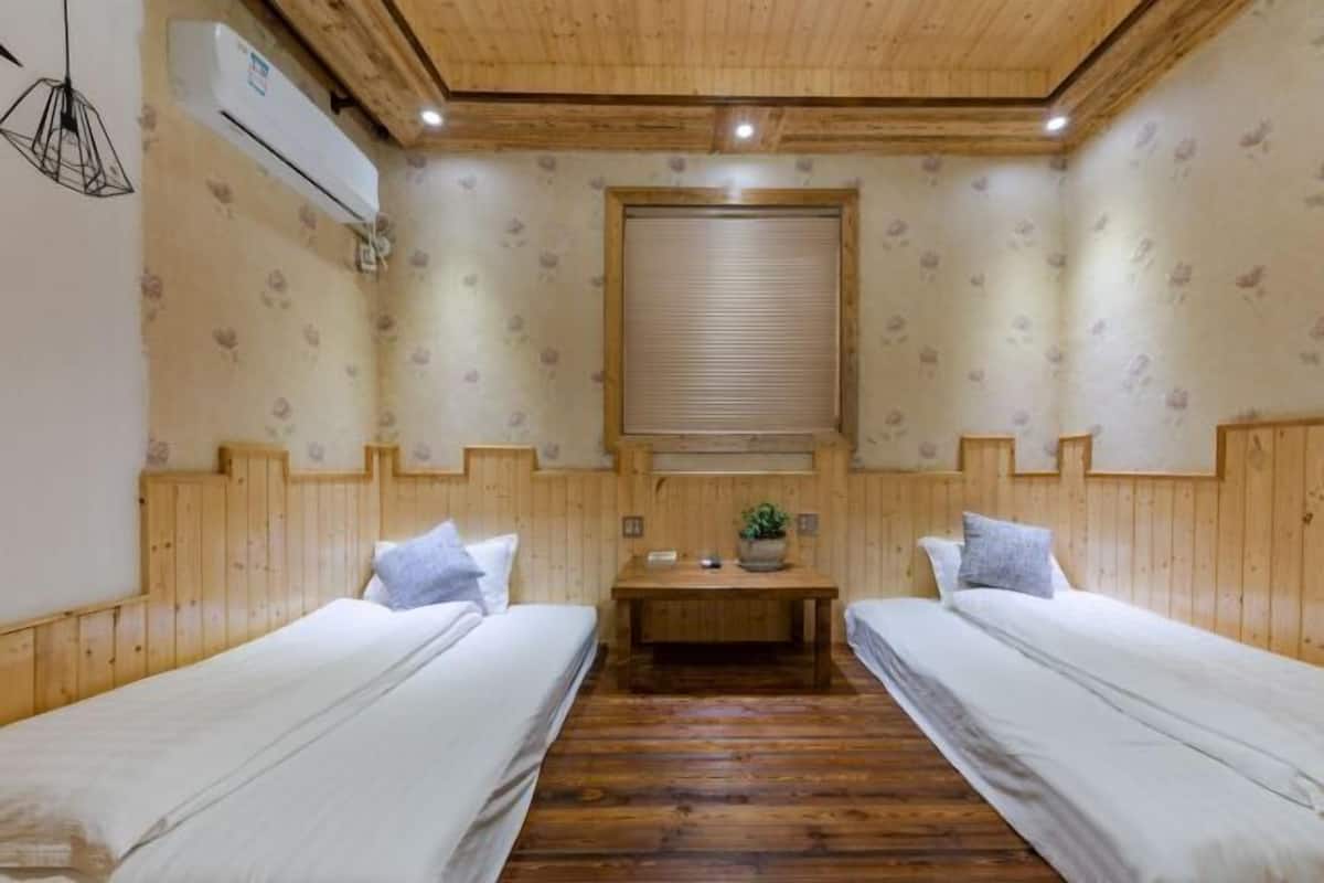A room with two beds, wooden walls, a central table, and a window with blinds.