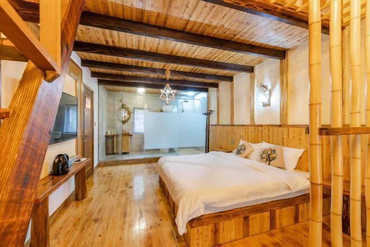 A wooden-floored bedroom with a bed, a bench, and a hanging light fixture.