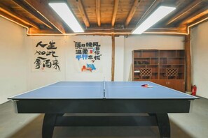 A ping pong table in a room with wooden beams on the ceiling, a fire extinguisher, and a wall with Japanese characters. - Moganshan Yingju Villa (Deqing)