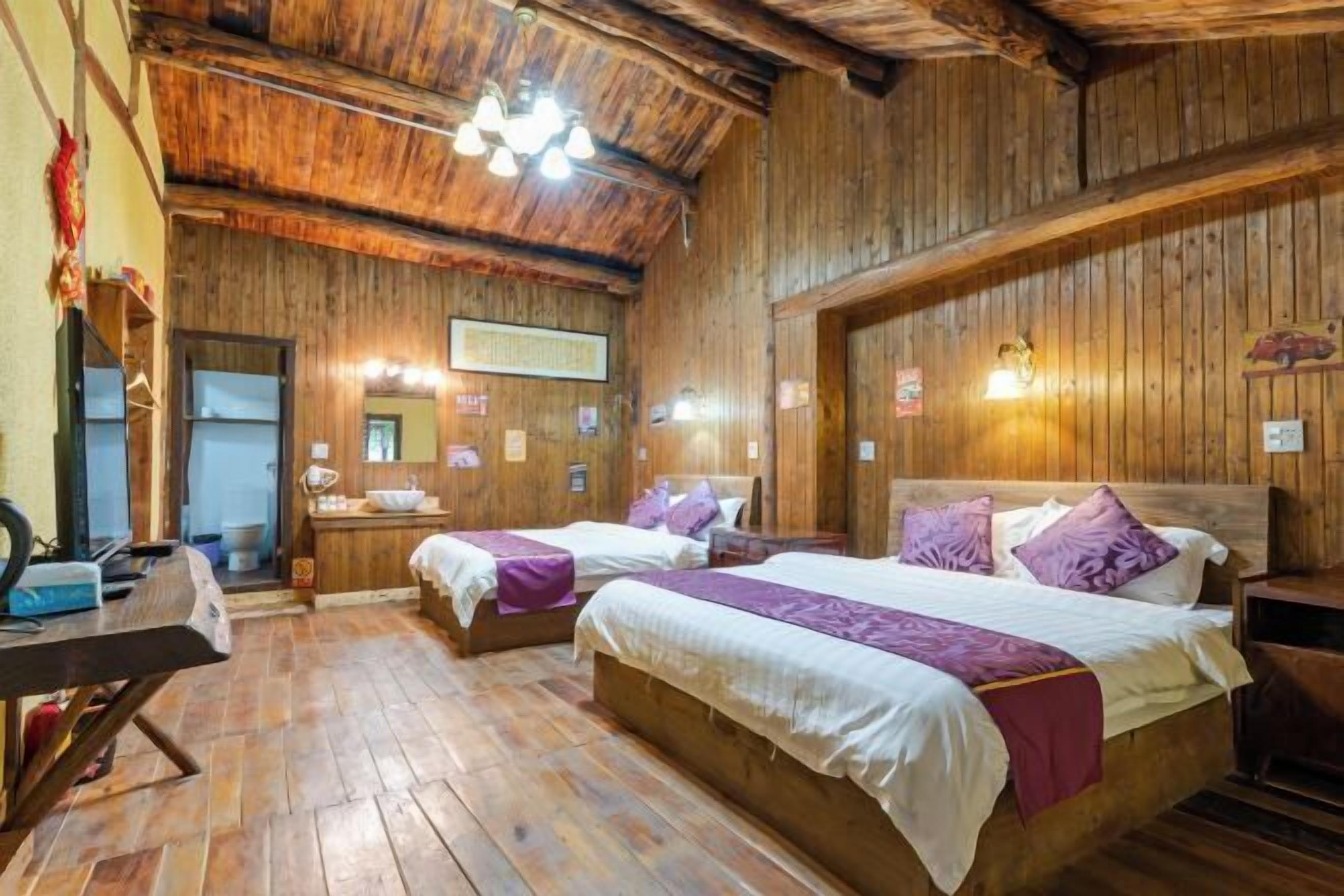 A wooden room with two beds, a wooden desk, and a bathroom visible through an open door.