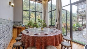 A round table with a patterned tablecloth, surrounded by stools, in a room with large windows and a view of greenery. - Moganshan Yingju Villa (Deqing)