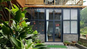 A modern building with large glass doors, a wooden balcony, and a stone-paved area with potted plants. - Moganshan Yingju Villa (Deqing)
