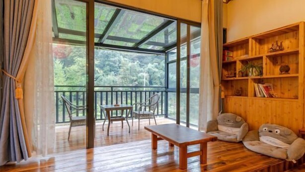 A wooden deck with a table and chairs, a wooden bookshelf, and a large sliding glass door leading to a balcony. - Moganshan Yingju Villa (Deqing)