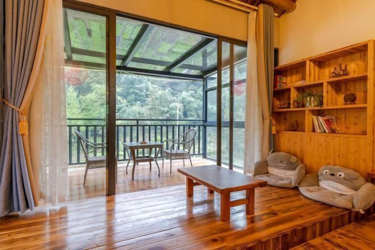 A wooden deck with a table and chairs, a wooden bookshelf, and a large sliding glass door leading to a balcony.