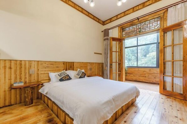 Ein Schlafzimmer mit Holzwänden, einem großen Bett, einem Nachttisch und einem Fenster mit Blick ins Freie.