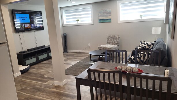 A modern living room with a dining area, a flat-screen TV mounted on the wall, a standing fan, and a window with blinds. - Practical-ly home
2 bedroom  quiet and peaceful suite.
tons of natural light
 (Edmonton)