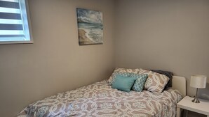 A bedroom with a bed, patterned bedding, a nightstand with a lamp, and a painting on the wall. - Practical-ly home
2 bedroom  quiet and peaceful suite.
tons of natural light
 (Edmonton)