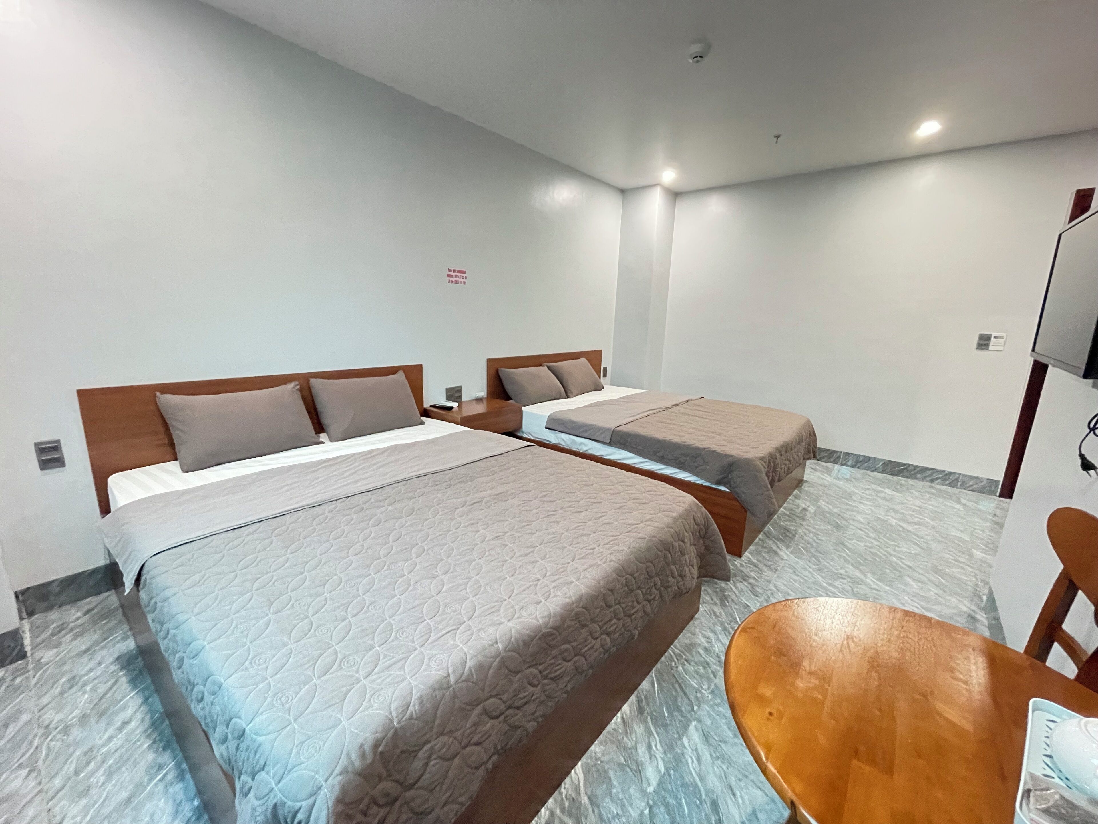 Una habitación de hotel con dos camas, cabecera de madera, una mesita y televisor.