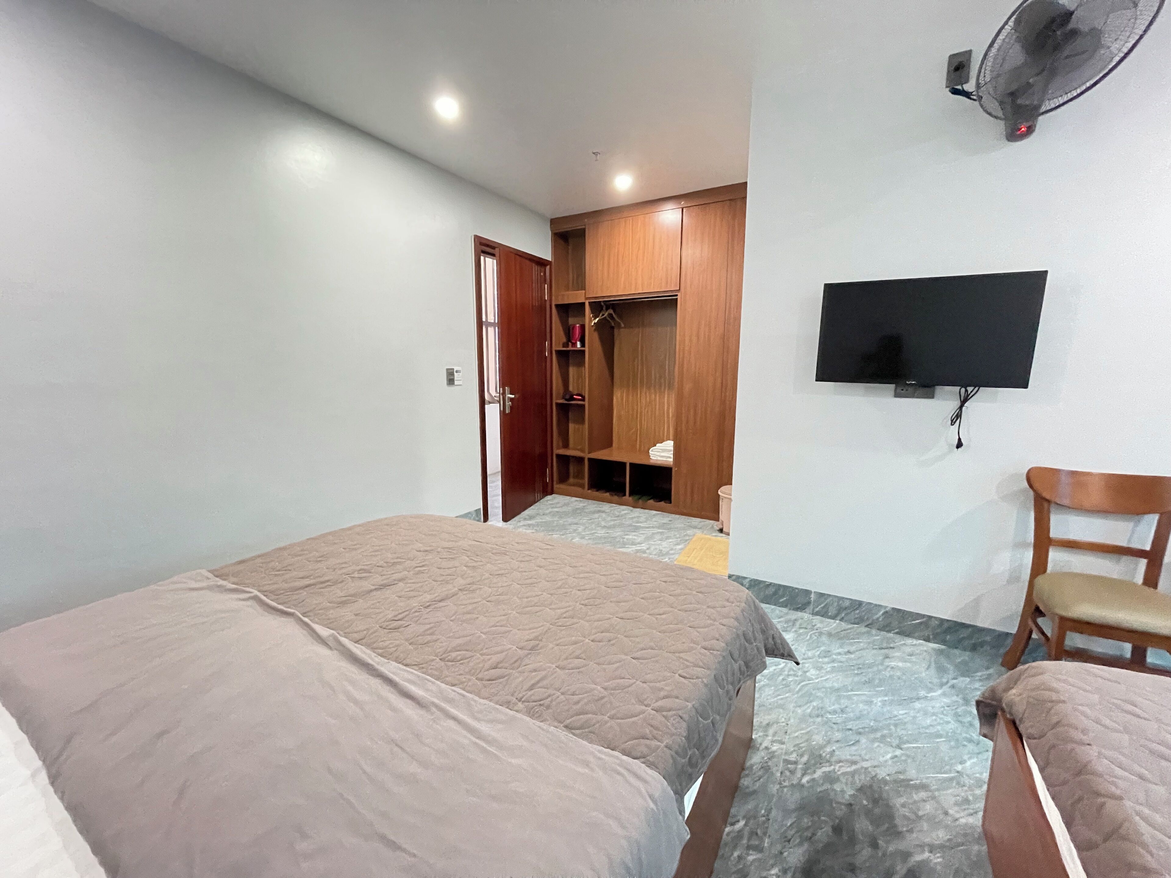 Un dormitorio con dos camas, un armario de madera, un televisor montado en la pared y una silla.
