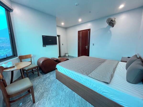 A hotel room with a bed, a desk with a chair, a television, and a window with a view. - Như Ý Hotel (Ha Giang 1)