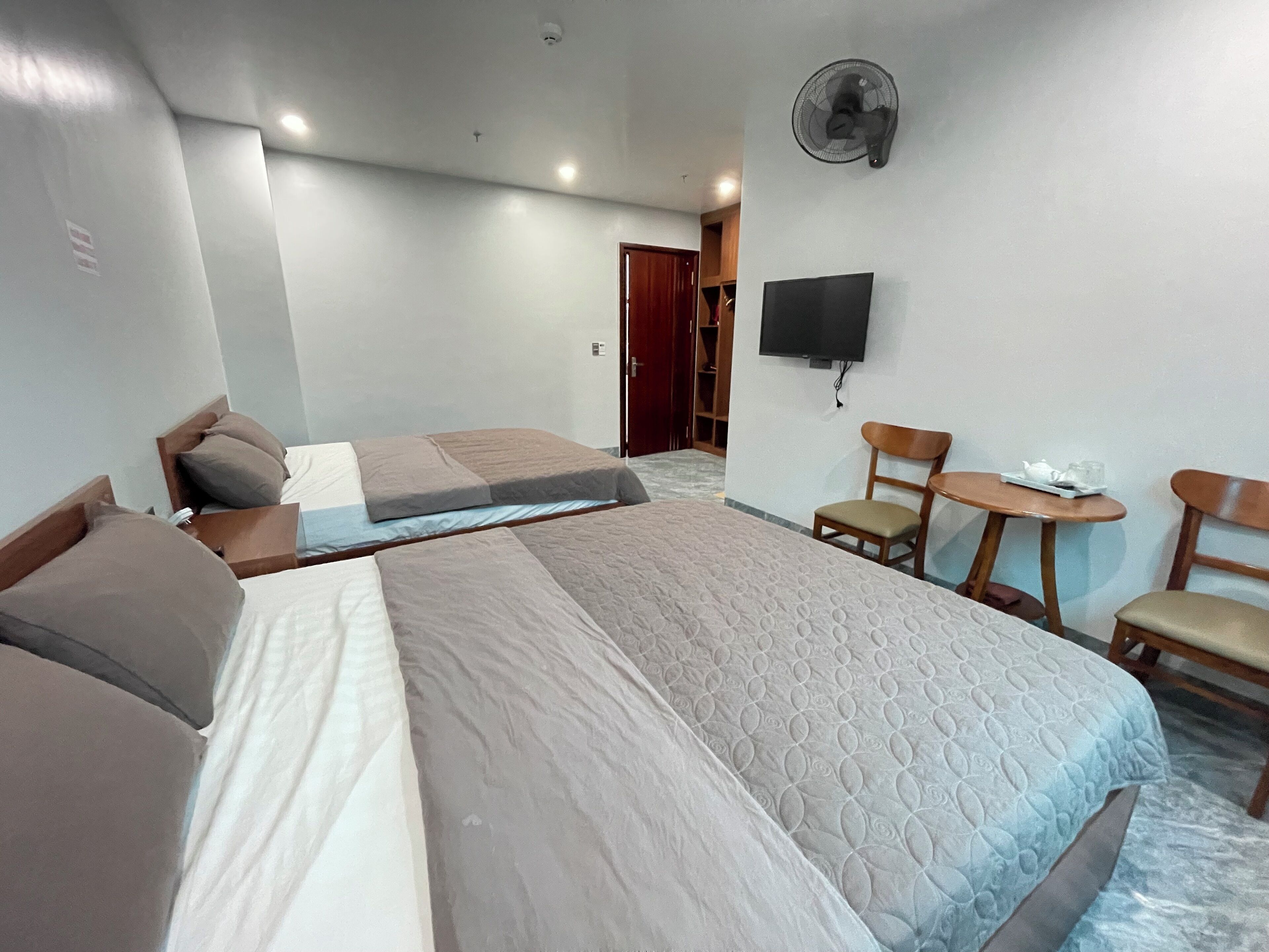 Une chambre d’hôtel avec deux lits, une télévision, un ventilateur et une petite table avec une chaise.