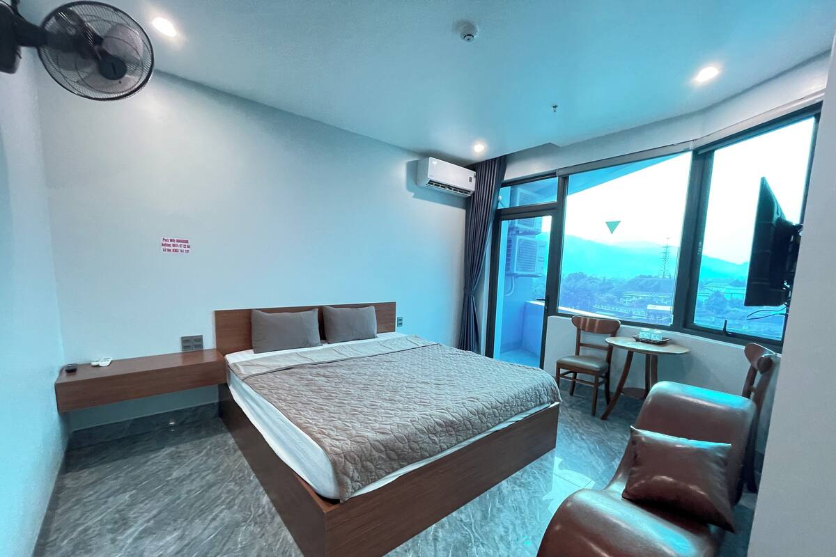 A modern hotel room with a large bed, a desk, a chair, and a view of the city.