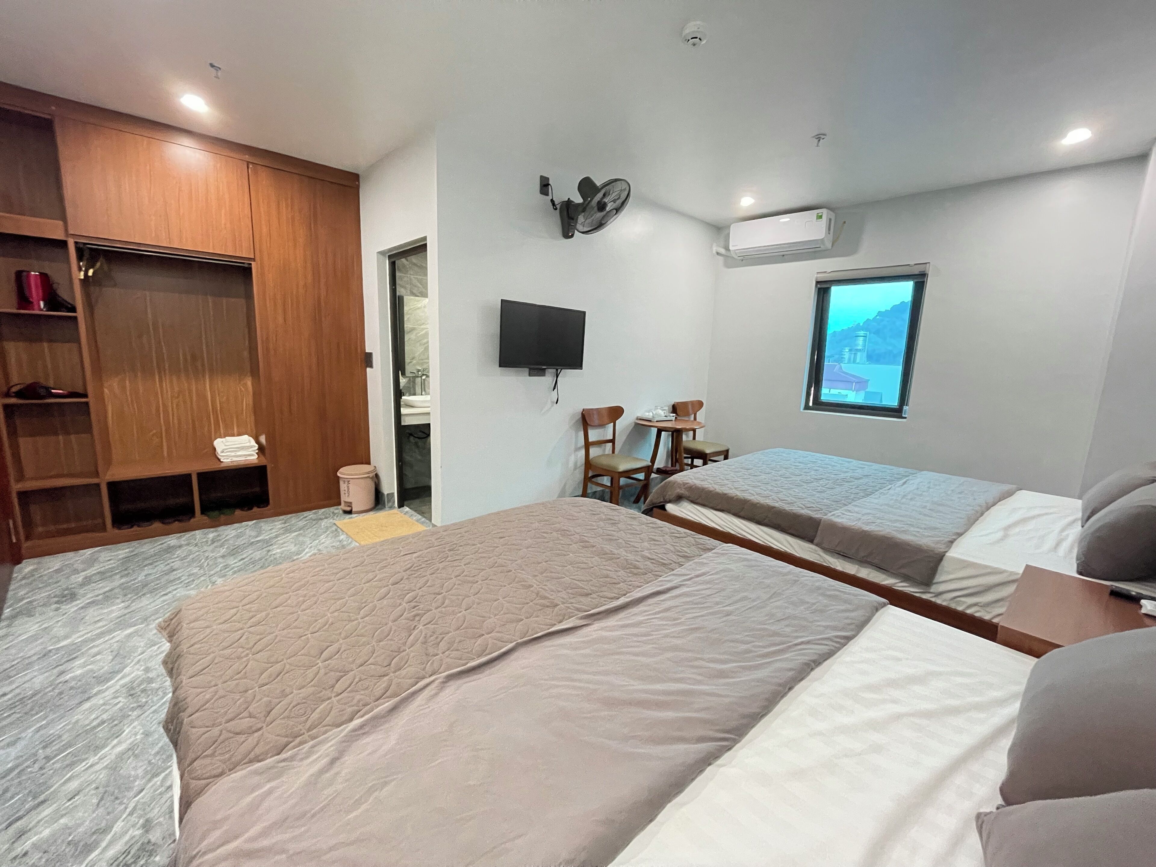 A hotel room with two beds, a wooden wardrobe, a TV, and a window with a view.