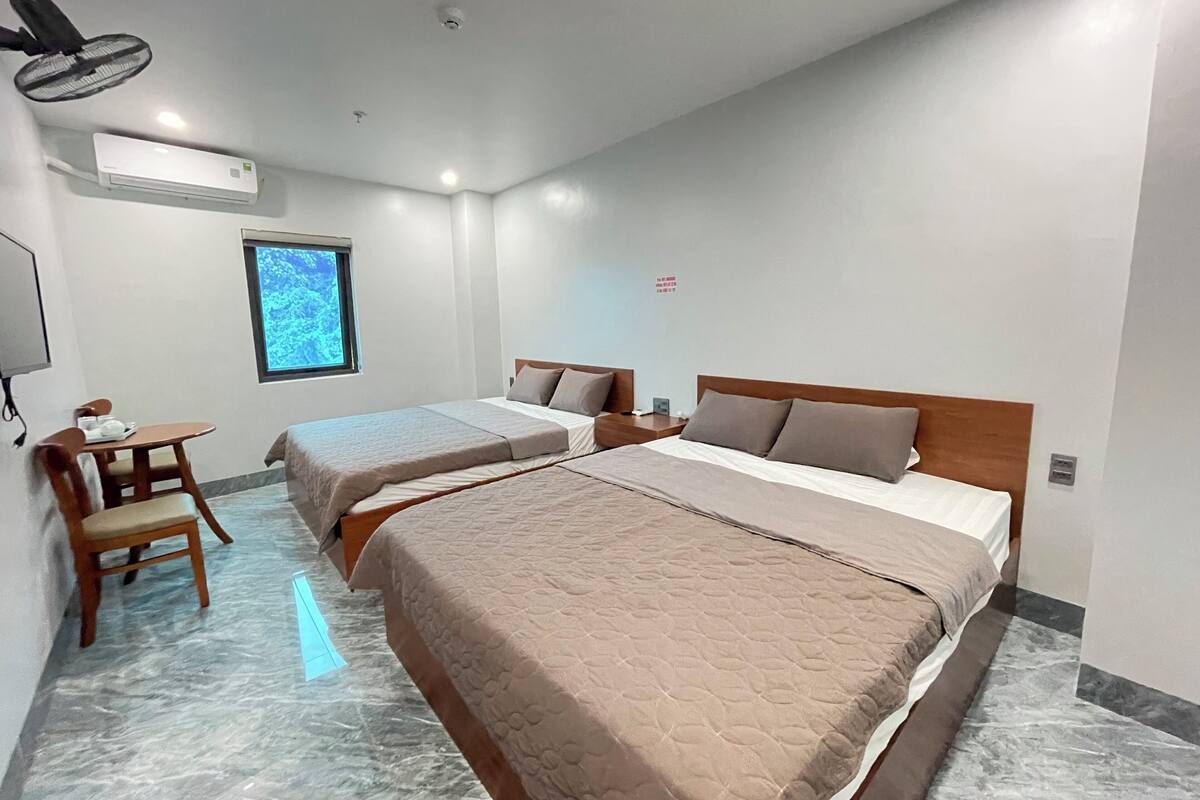 A hotel room with two beds, a desk, a chair, and a window with a view.
