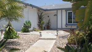 A pathway leading to a house with a white exterior, surrounded by various plants and a gravel area.