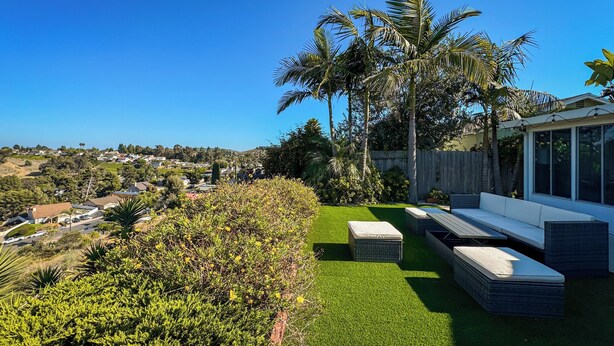 A modern outdoor patio with a view of a residential area, including a wooden fence and palm trees.