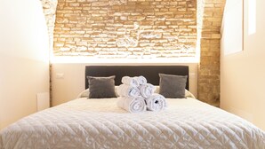 A neatly made bed with rolled towels, two pillows, and a stone wall behind it.