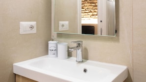 A bathroom with a white sink, a mirror, and a stone wall.