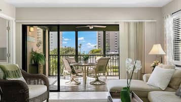 A modern living room with a sofa, a dining table with chairs, a balcony with a view of the city, and a potted plant.