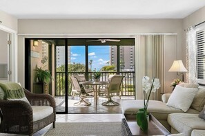 A modern living room with a sofa, a dining table with chairs, a balcony with a view of the city, and a potted plant.